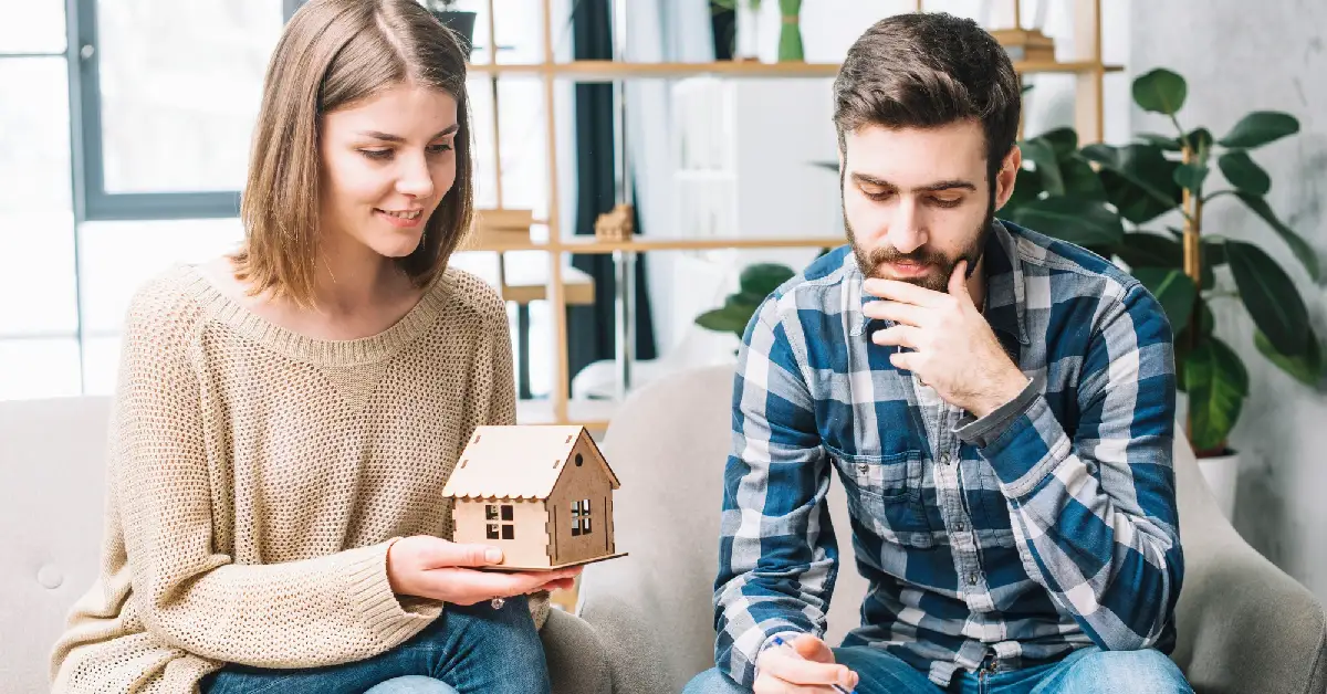 Young couple examining a small house model while discussing home selling tips for first-time sellers