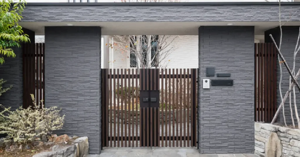 Modern minimalist house front design idea featuring dark gray stone facade, wooden slatted gate entrance, and strategic landscaping elements